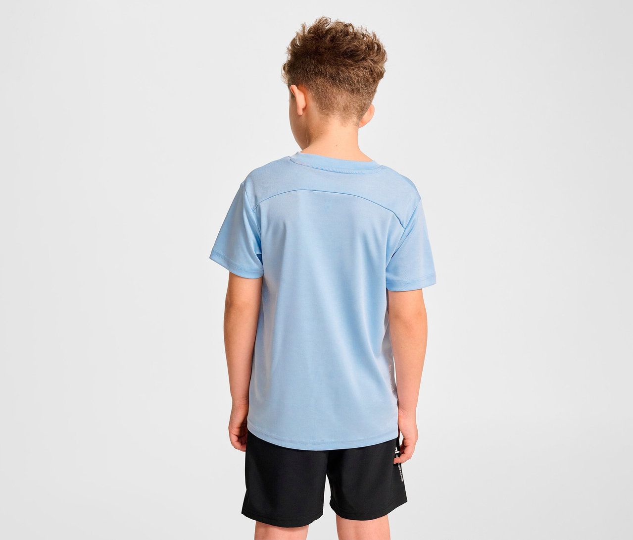 Junge von hinten trägt hellblaues HUMMEL HMLJR pulse Trainings-T-Shirt und schwarze Shorts.