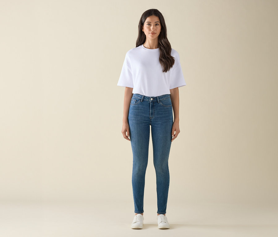 Eine Frau steht in einem weißen T-Shirt, blauen Jeans und weißen Turnschuhen.
