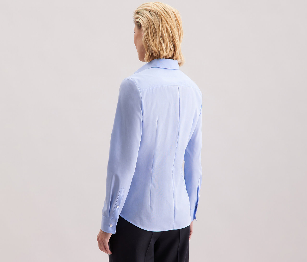 Rückansicht einer Frau mit blonden, schulterlangen Haaren, die eine hellblaue Seidensticker Bluse Slim Fit non iron trägt.
