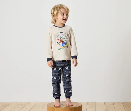 Ein Junge steht auf einem Holzsockel und trägt einen Disney-Pyjama.