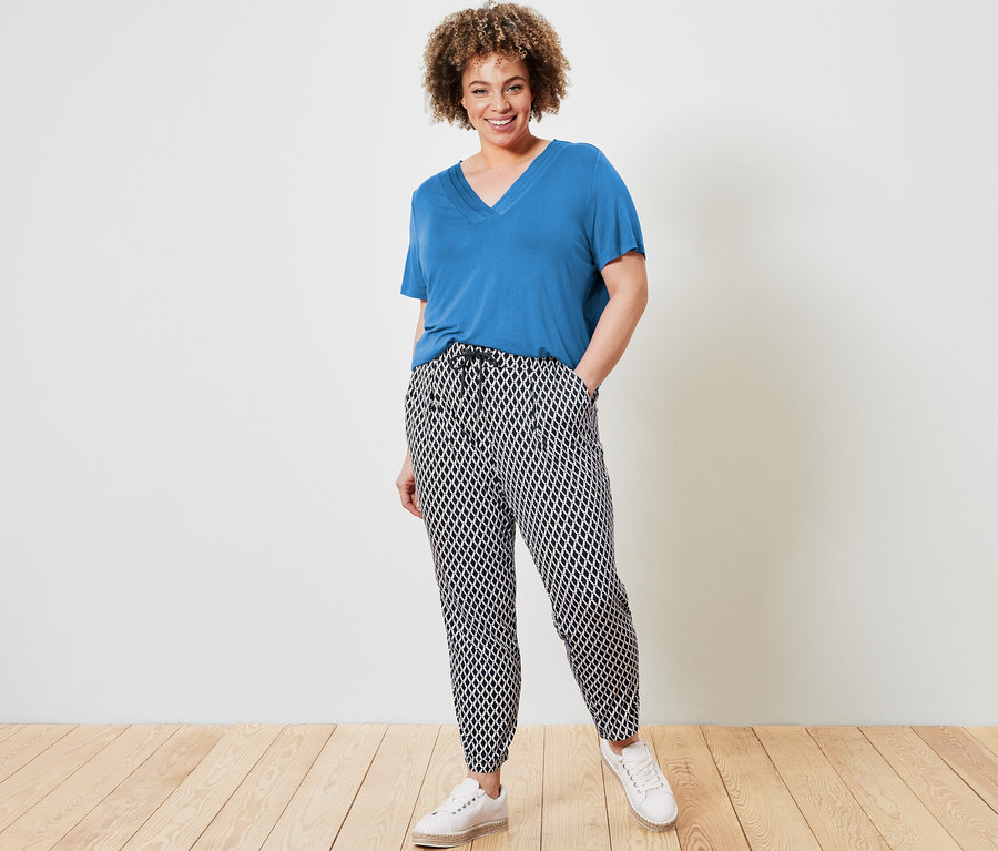 Frau posiert in kobaltblauem Shirt mit Faltendetail und bedruckter Jerseyhose.