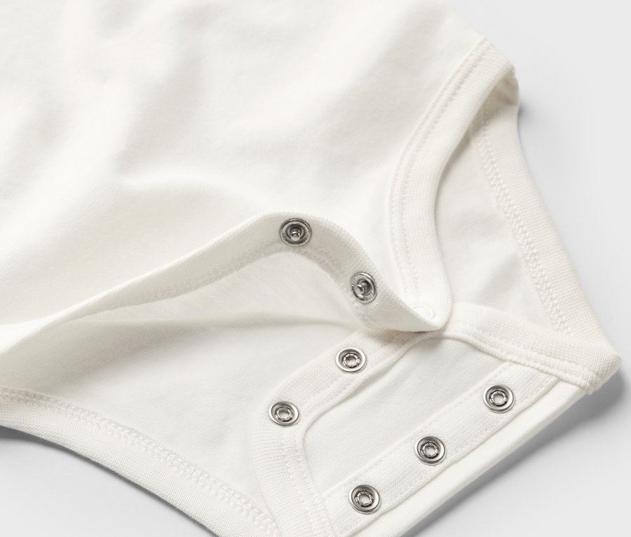 Detailansicht eines weißen Baby-Bodys mit Mitwachsfunktion und Druckknöpfen.