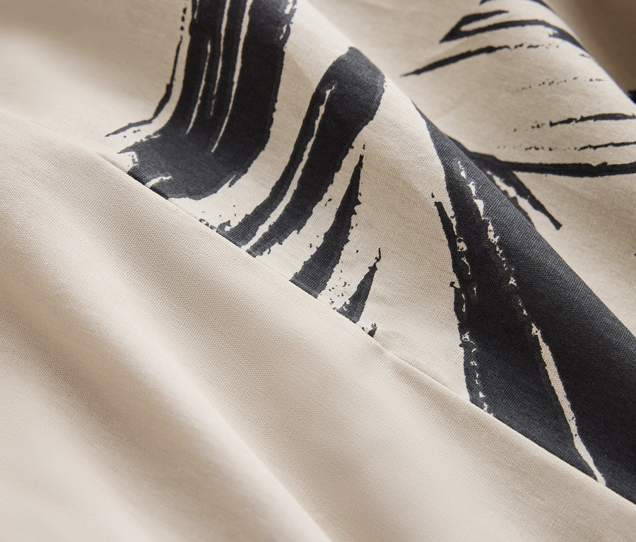 Detailaufnahme eines cremefarbenen Stoffes mit dunkelblauem abstraktem Muster.