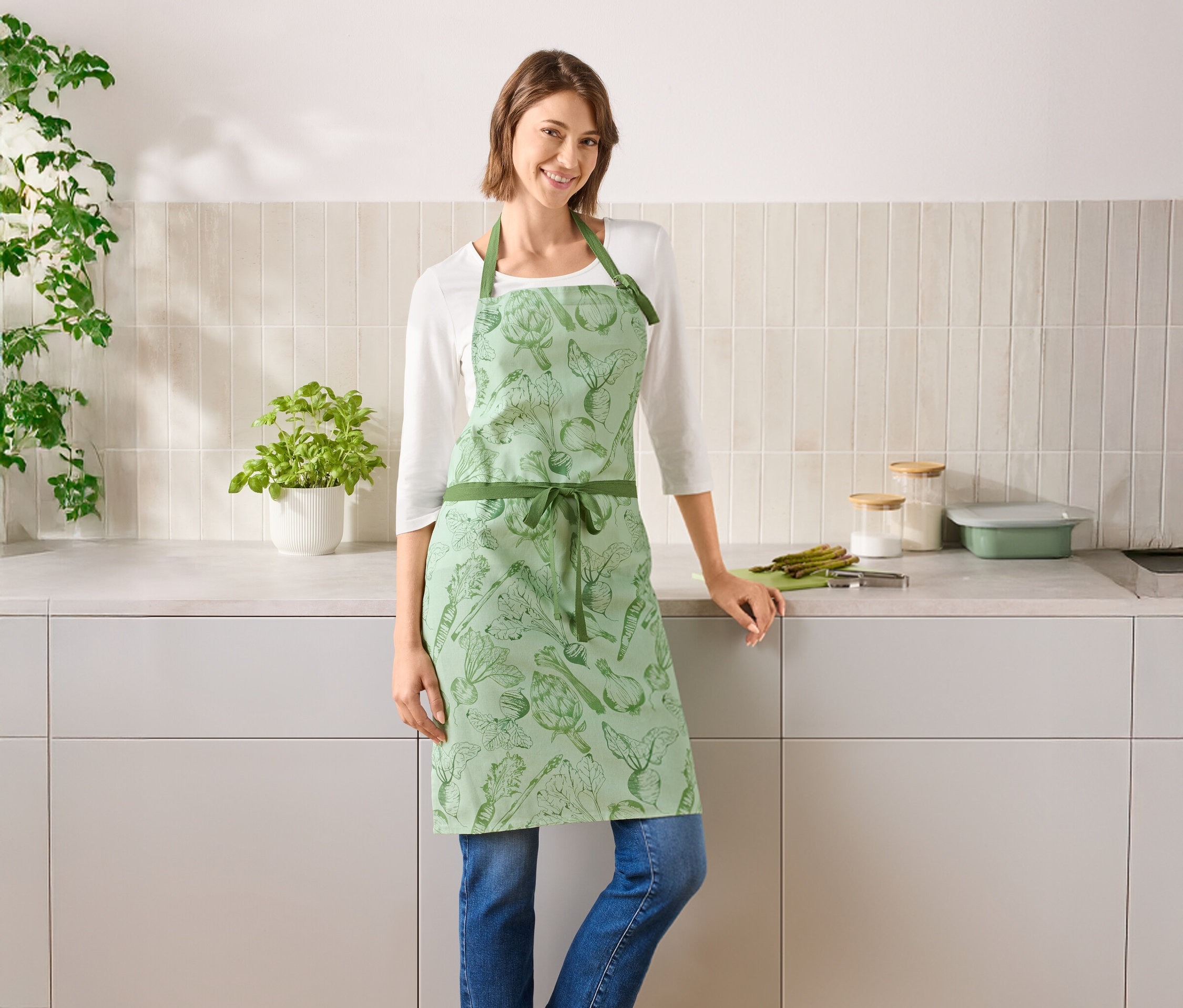 Eine Frau steht in einer Küche und trägt eine grüne Gemüseschürze.