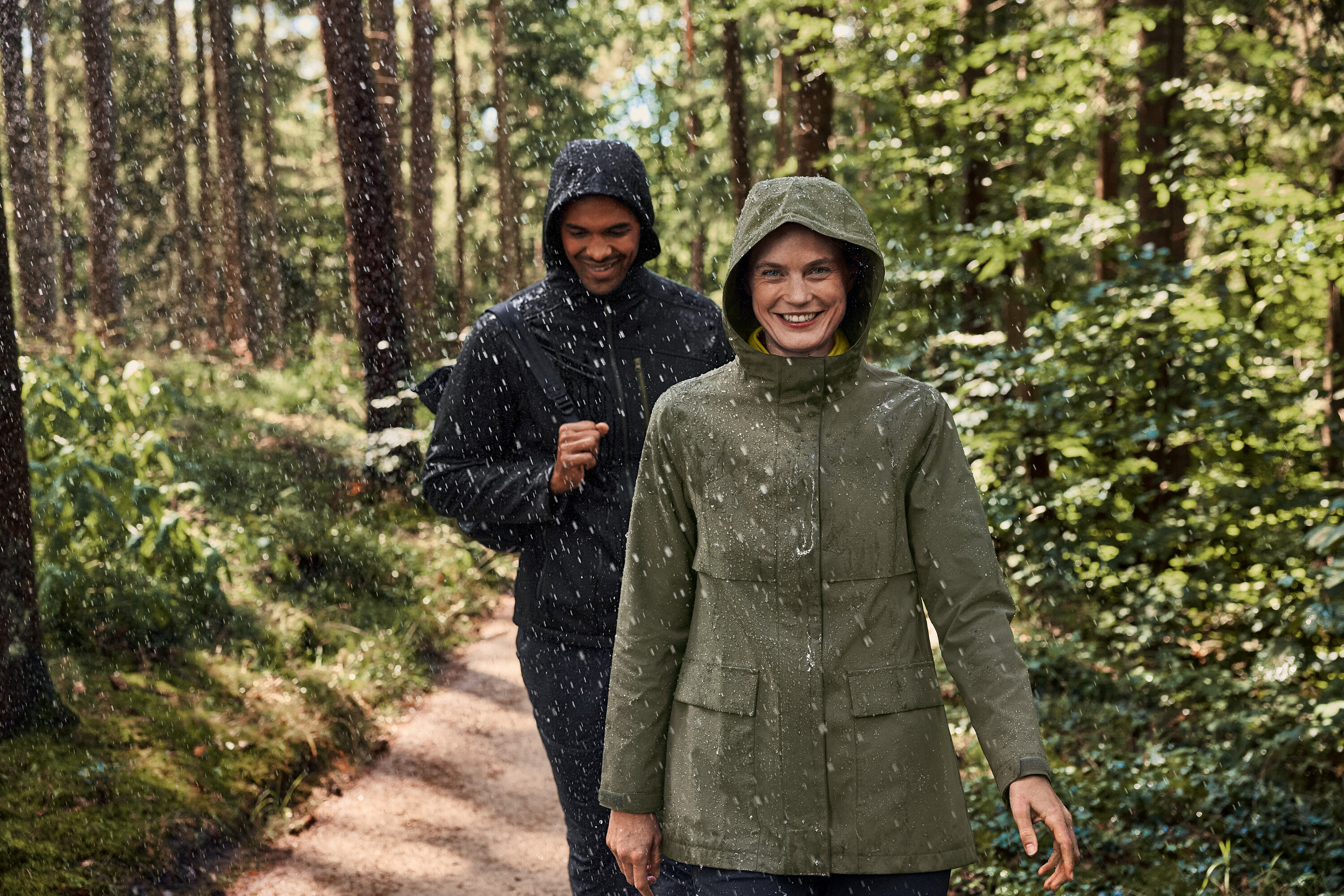 Zwei Personen gehen im Regen durch den Wald. Die Frau trägt einen khaki-anthrazitfarbenen Fleece-Troyer.