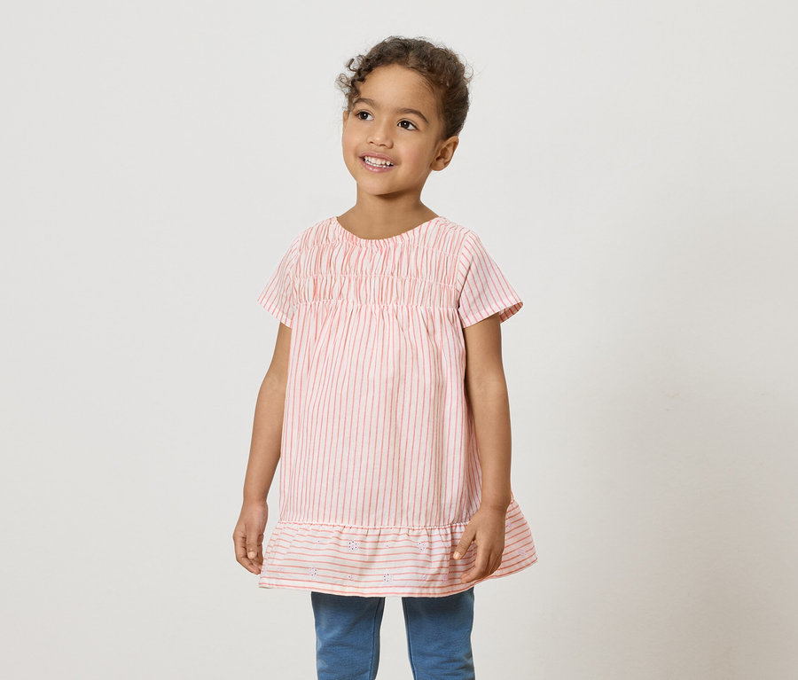 Ein lächelndes junges Mädchen trägt ein rosa-weiß gestreiftes Hemd und blaue Jeans.
