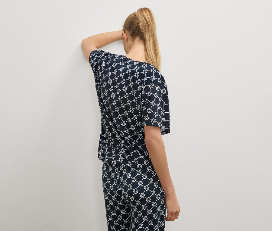 Frau mit blonden Haaren trägt einen marineblauen Pyjama mit weißem Muster.