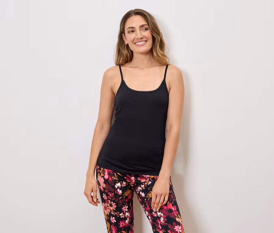 Frau mit langen Haaren, die ein schwarzes Tanktop mit Spaghettiträgern und eine blumengemusterte Hose trägt.