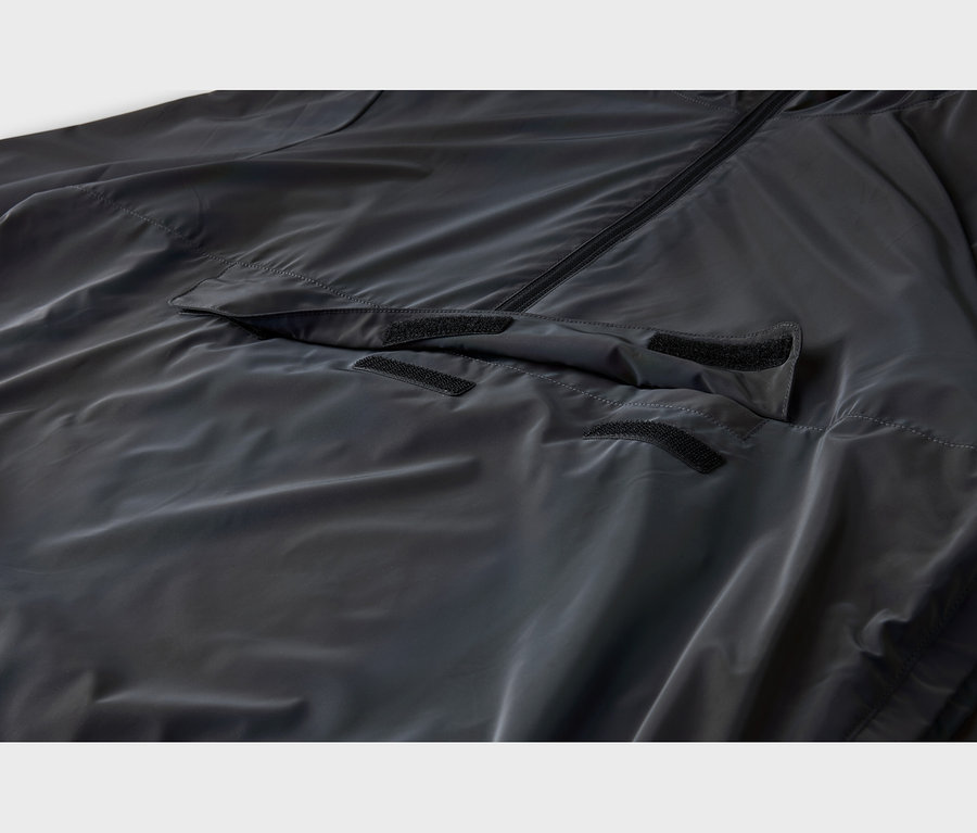 Dunkelgraue, leicht glänzende Jacke mit schwarzem Reißverschluss und einer vorderen Pattentasche mit drei schwarzen Klettverschlüssen.