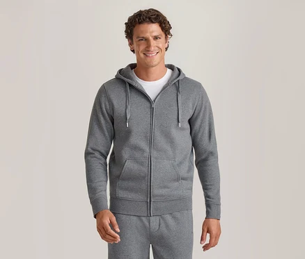 Lächelnder Mann in einem grauen Kapuzenpullover mit Reißverschluss über einem weißen T-Shirt und passender grauer Jogginghose.