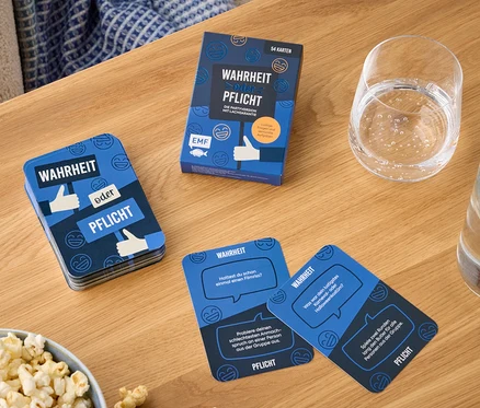 Auf einem Holztisch liegen eine Schüssel Popcorn, ein Glas Wasser und eine Packung Spielkarten namens „Wahrheit oder Pflicht“.