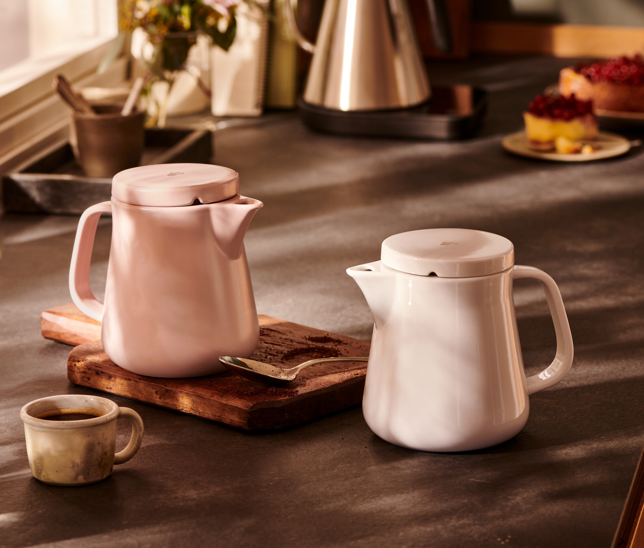 Zwei Kaffeebereiter aus Keramik, weiß und rosa, stehen nebeneinander auf einem Holzbrett.