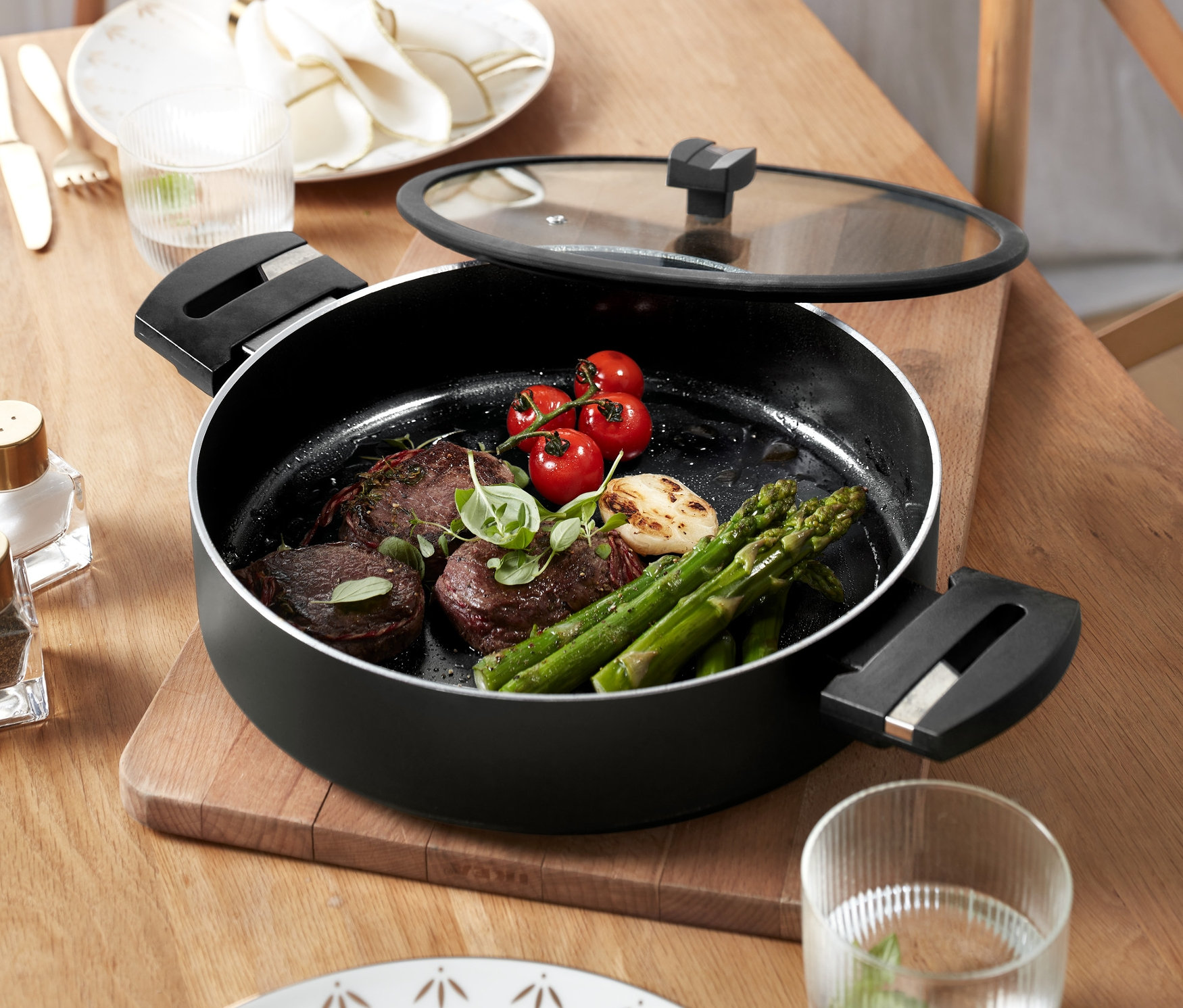 Servierpfanne mit Glasdeckel »Alu Recycled Induction b.green« mit Steak, Spargel und Tomaten steht auf einem Holztisch.