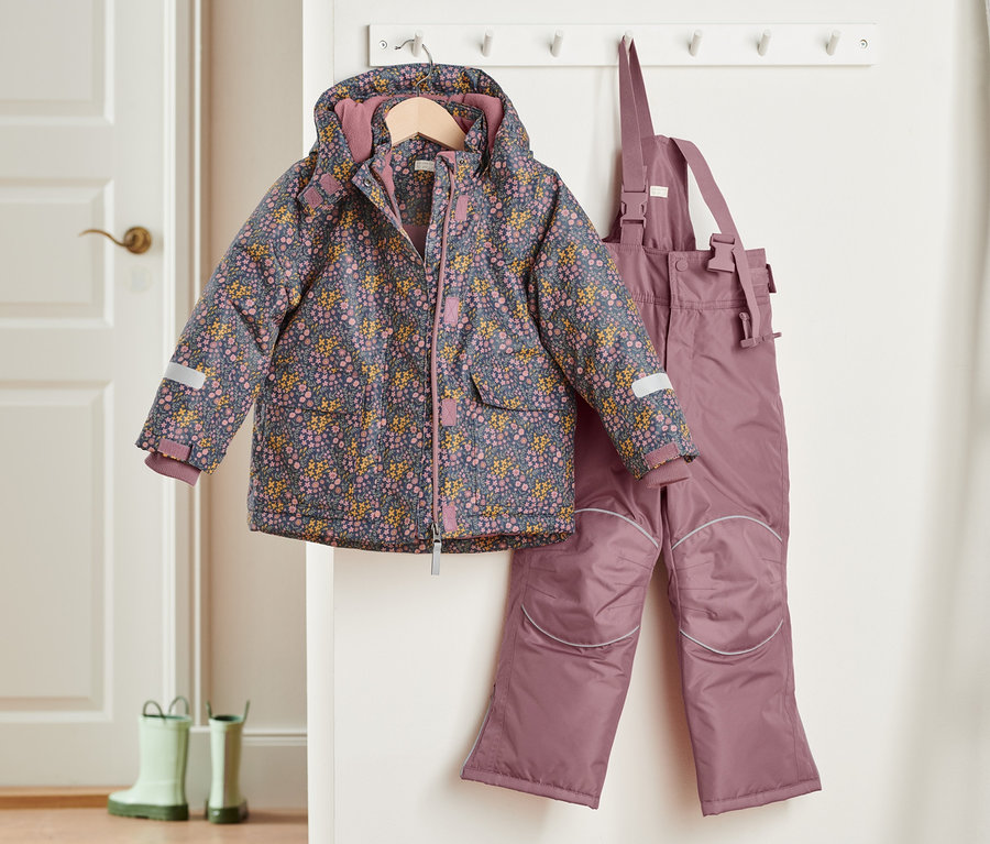 Eine 2-teilige Schneekombi in Rosa hängt an einer Garderobe, eine blumengemusterte Jacke und eine Latzhose.