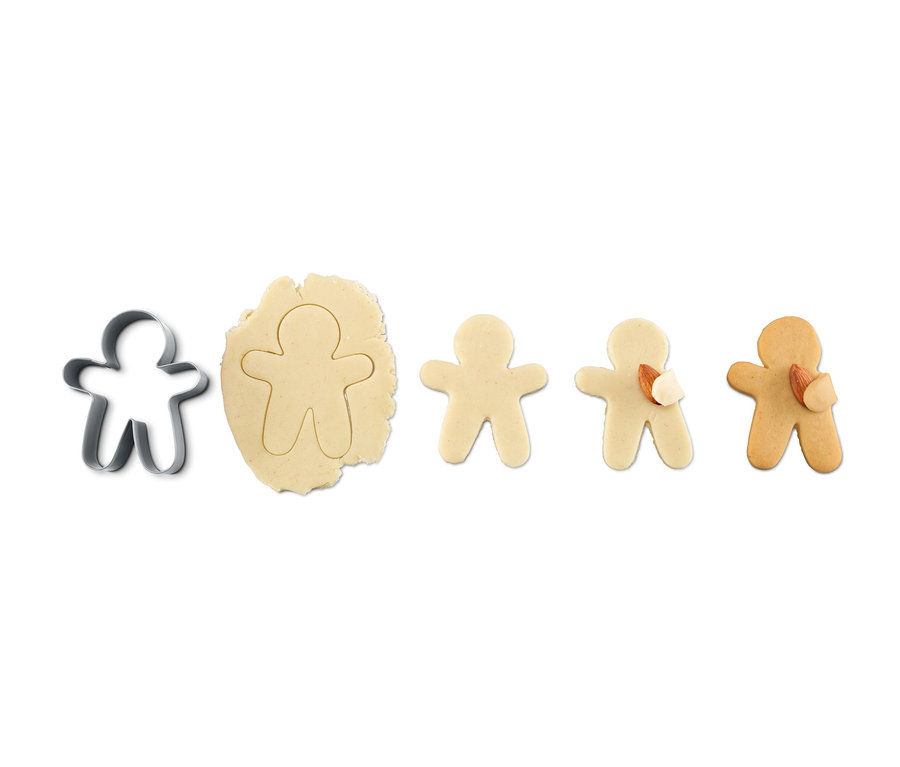 Kuschelkeks-Ausstecher neben Teig mit Lebkuchenmannform und drei gebackenen Lebkuchen.