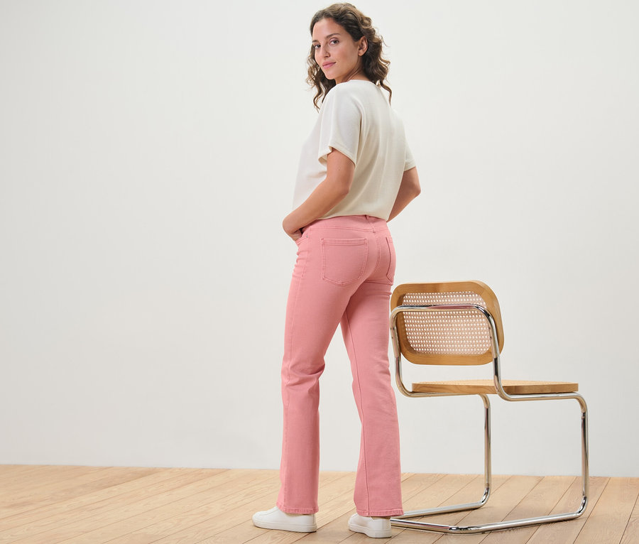 Frau posiert in korallenroten Bootcut Jeans ‒ Fit »Lou« neben einem Stuhl.