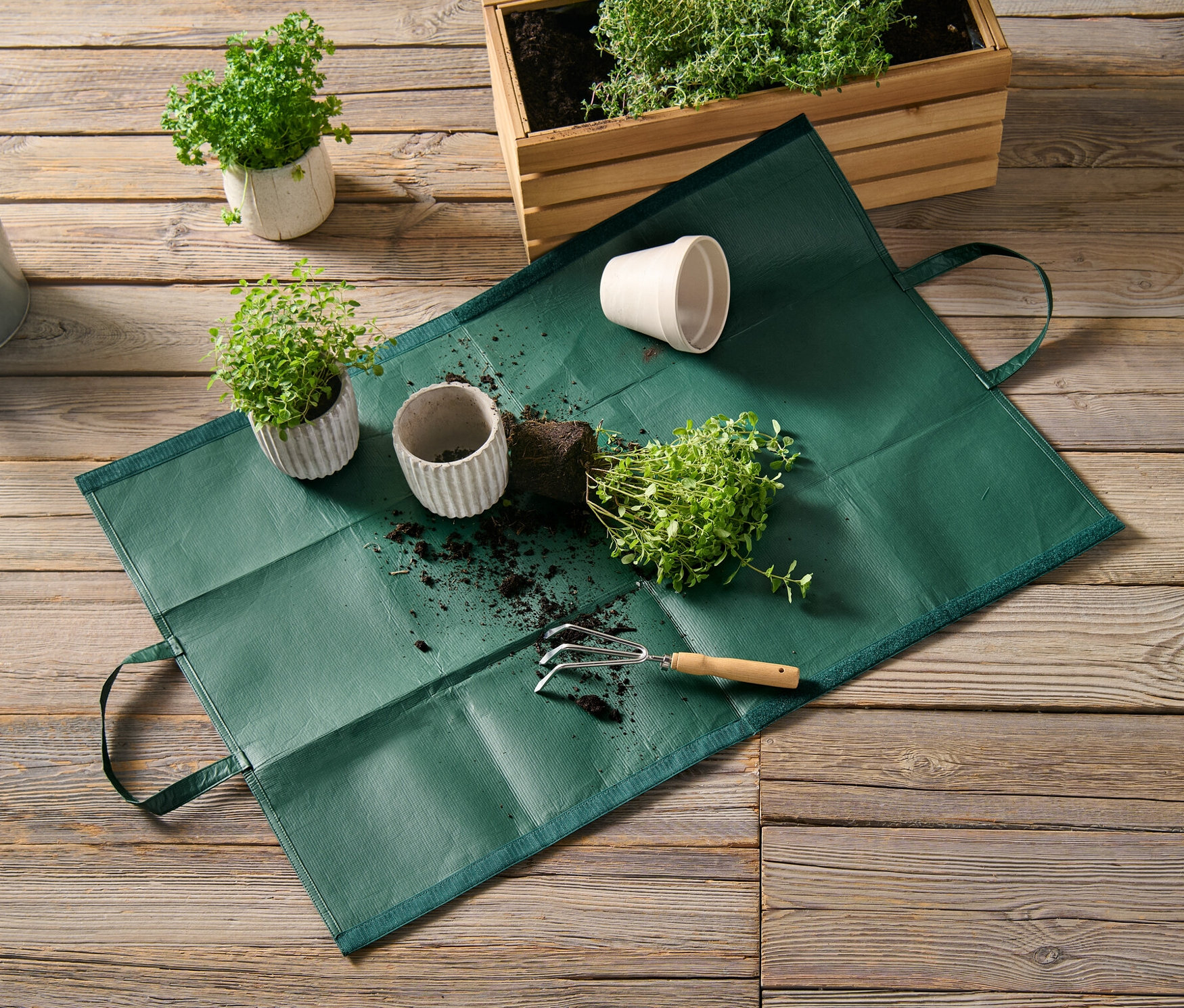 Eine Gartenabfalltasche liegt auf einem Holzboden neben Topfpflanzen und einer Gießkanne.