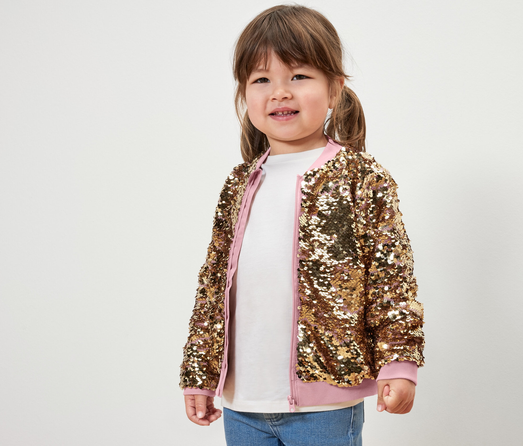 Ein lächelndes kleines Mädchen posiert in einer Kinder-Paillettenjacke.