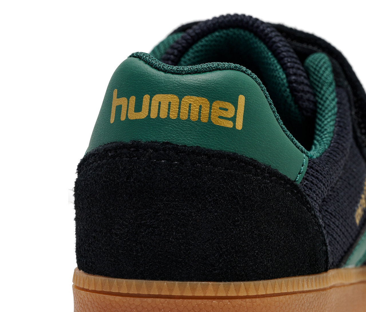 Detailaufnahme eines HUMMEL VM78 CPH JR Schuhs mit schwarzem Wildleder, dunkelblauem Strick und grünem Logo.