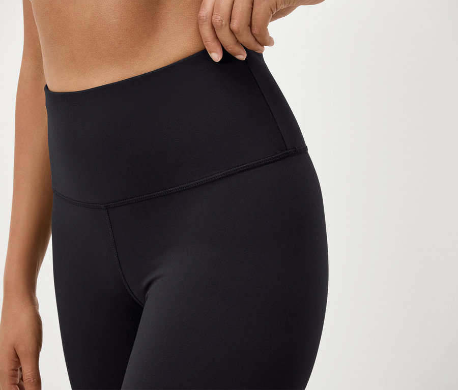 Detailaufnahme einer Frau, die schwarze, hochtaillierte Leggings trägt und den Bund anpasst.