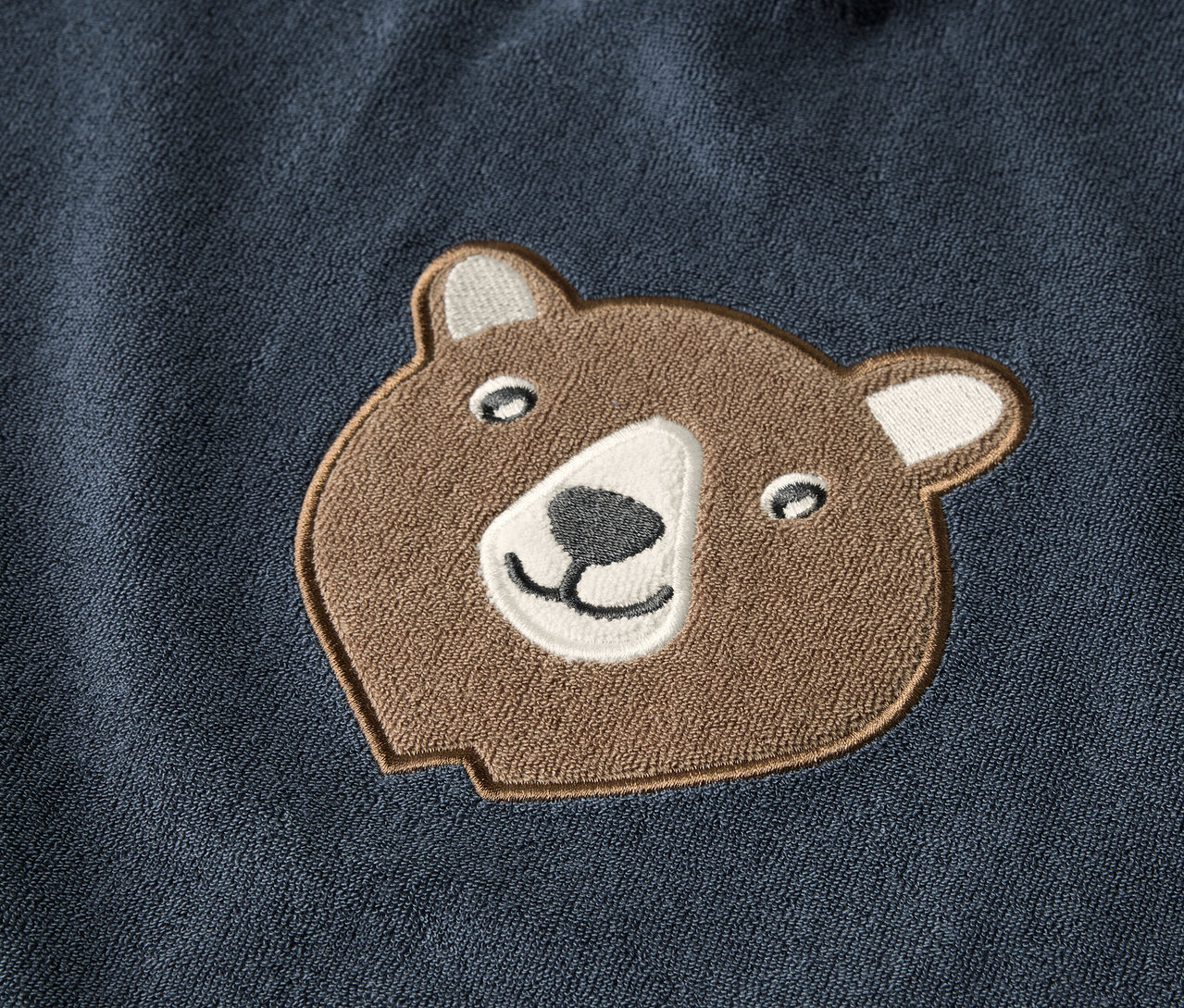 Detailansicht eines Kinder-Frottierponchos mit braunem Bärenkopf-Applikation.