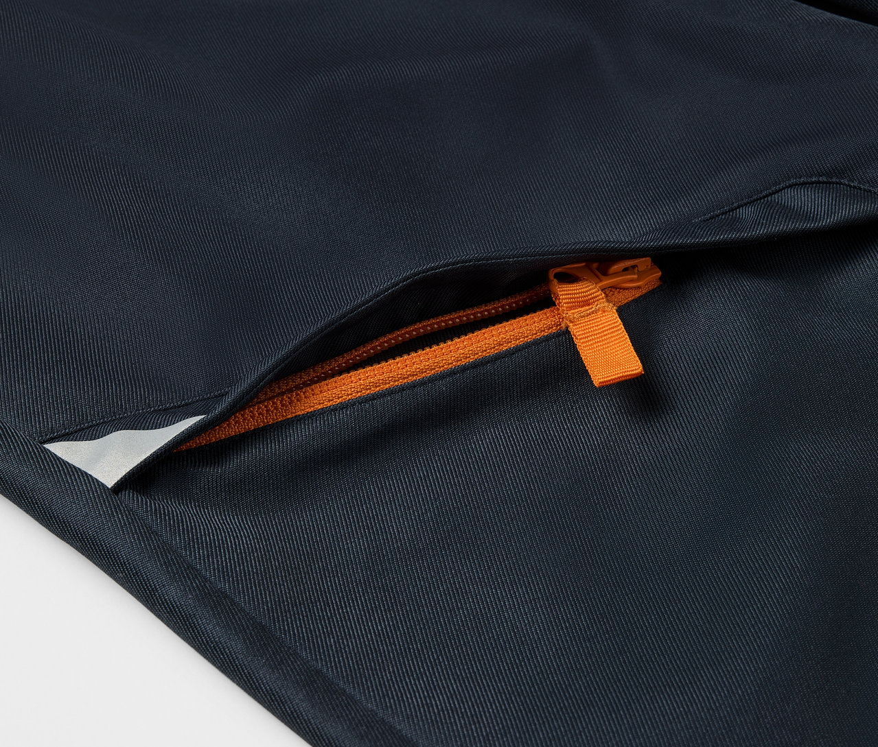 Detailaufnahme einer Kinder-Softshellhose mit orangefarbenem Reißverschluss an der Tasche.