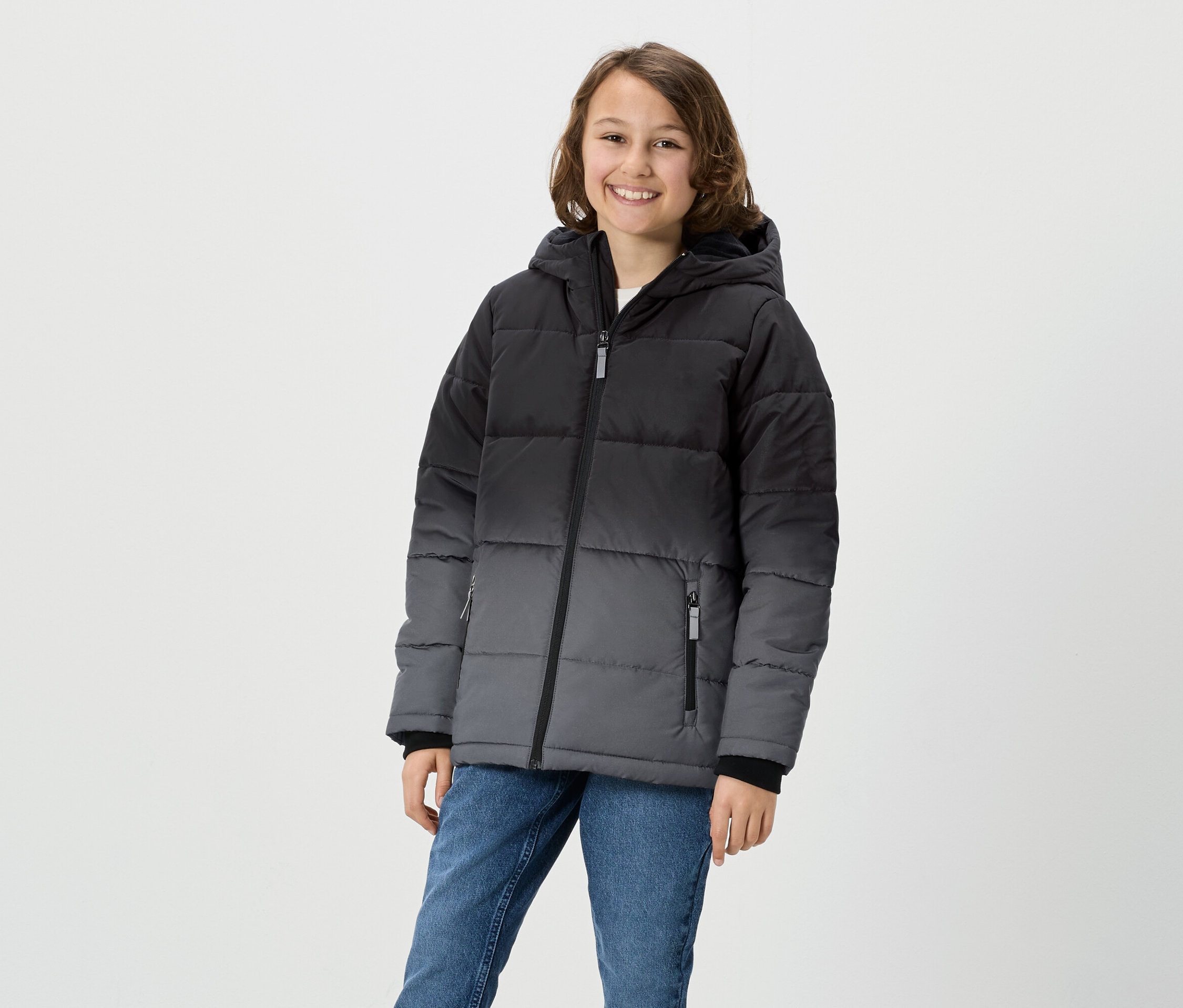 Mädchen posiert in grau-schwarzer Daunenjacke mit Kapuze und Jeans.