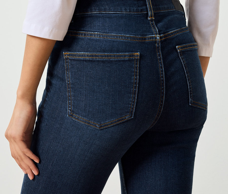 Nahaufnahme einer Frau von hinten, die dunkelblaue Jeans mit Taschen und braunen Nähten trägt.