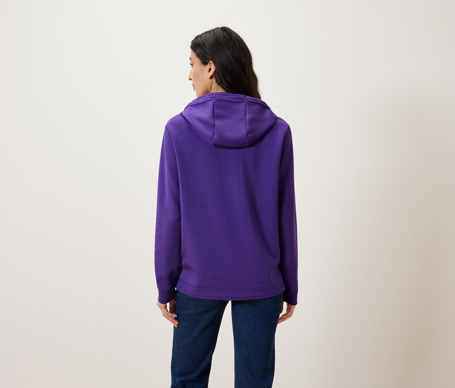 Eine Frau von hinten trägt einen violetten Hoodie und Jeans.
