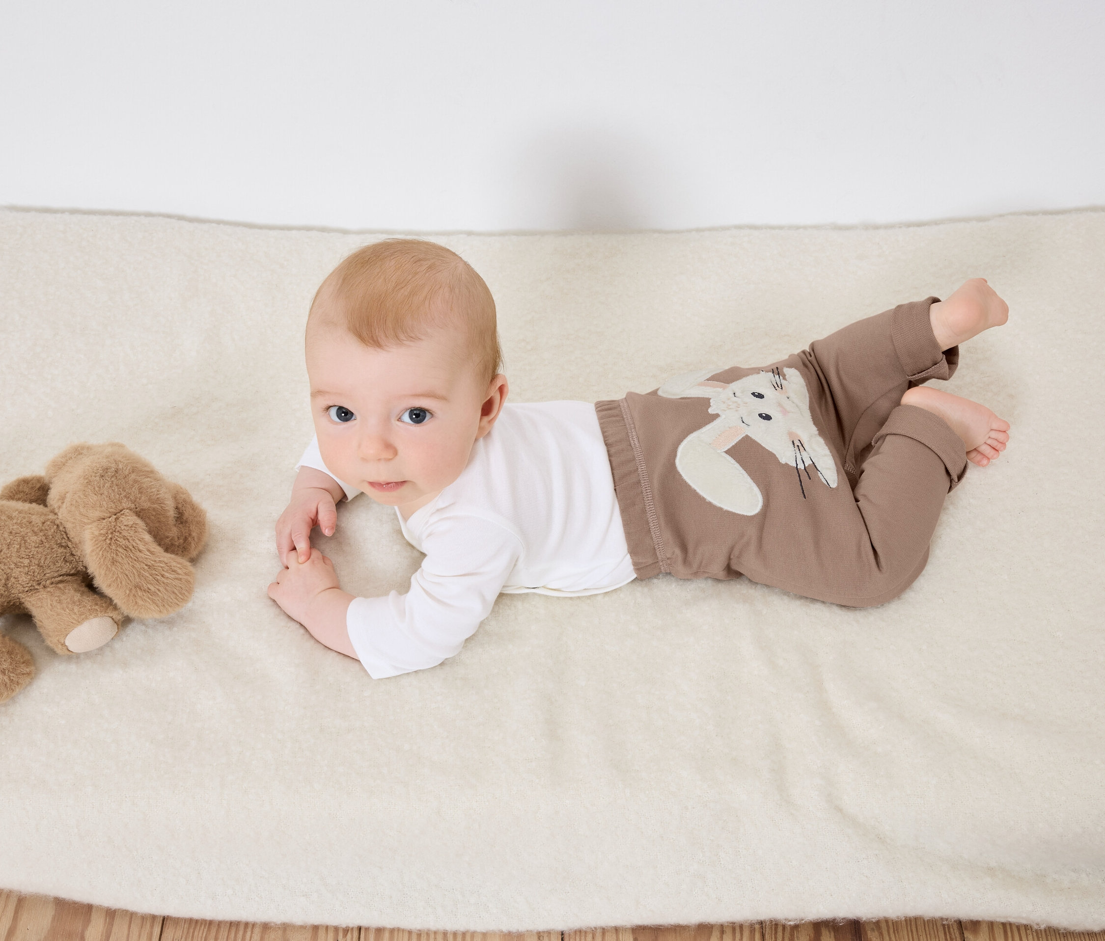 Baby liegt auf dem Bauch auf einer weißen Decke neben einem Plüsch-Elefanten.