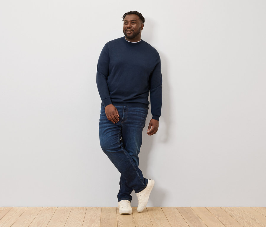 Mann posiert an einer Wand, trägt einen dunkelblau melierten Merino-Pullover.