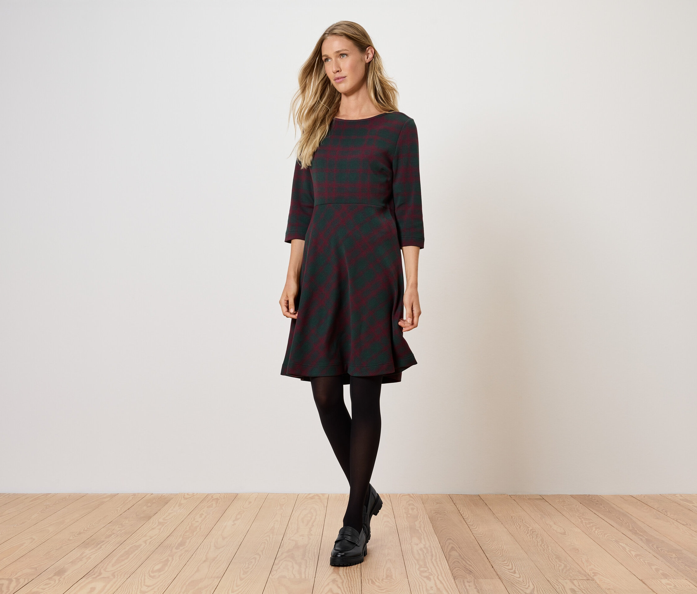 Frau posiert in grauem Kleid mit Dreiviertelärmeln und schwarzer Strumpfhose.