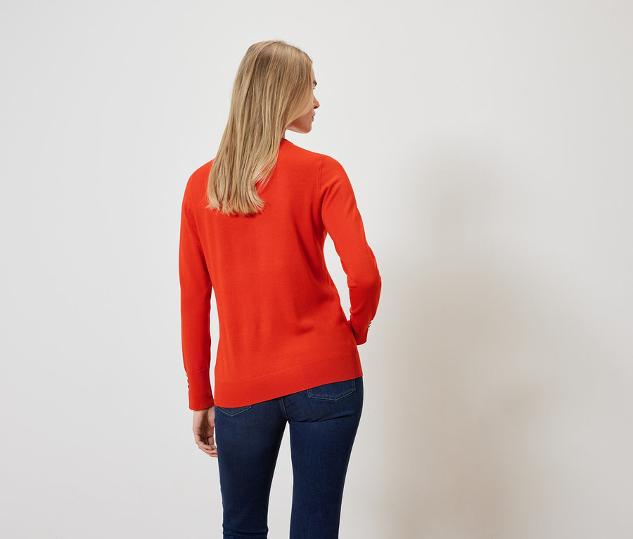 Rückansicht einer blonden Frau in orangefarbenem Pullover und dunkelblauen Jeans.