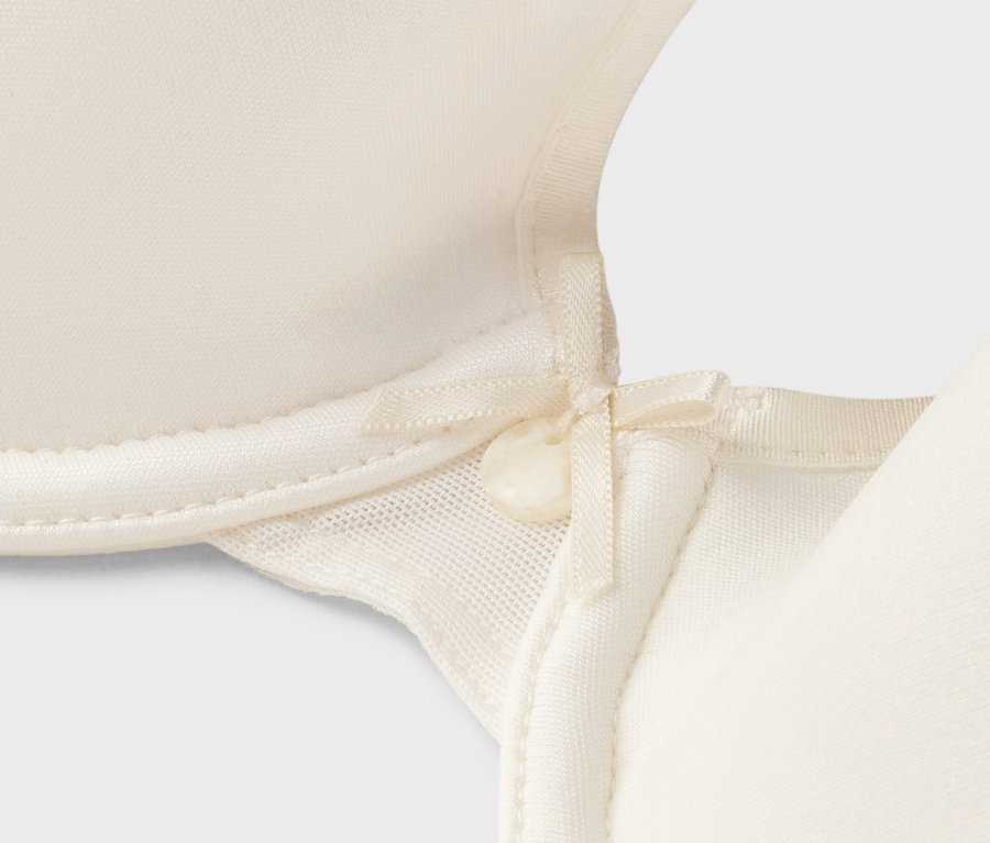Detailansicht eines cremefarbenen BHs mit Schleife.