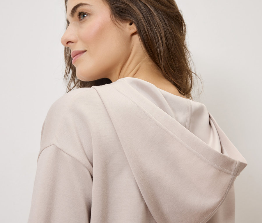 Frau trägt einen hellbraunen Kapuzenpullover.