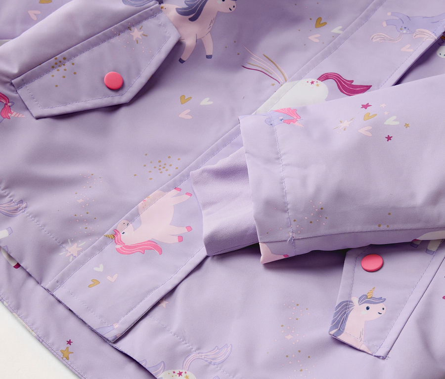Nahaufnahme einer lila Jacke mit Einhornmuster, einer Tasche mit einem pinken Knopf und einem Ärmel.