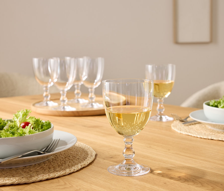 Auf einem Holztisch stehen Salatschüsseln und Weinkelche, einige mit Weißwein gefüllt.