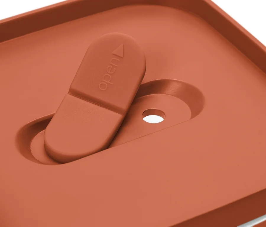 Detailaufnahme eines orangefarbenen Behälterdeckels mit Schiebeverschluss in der Position 'offen'.