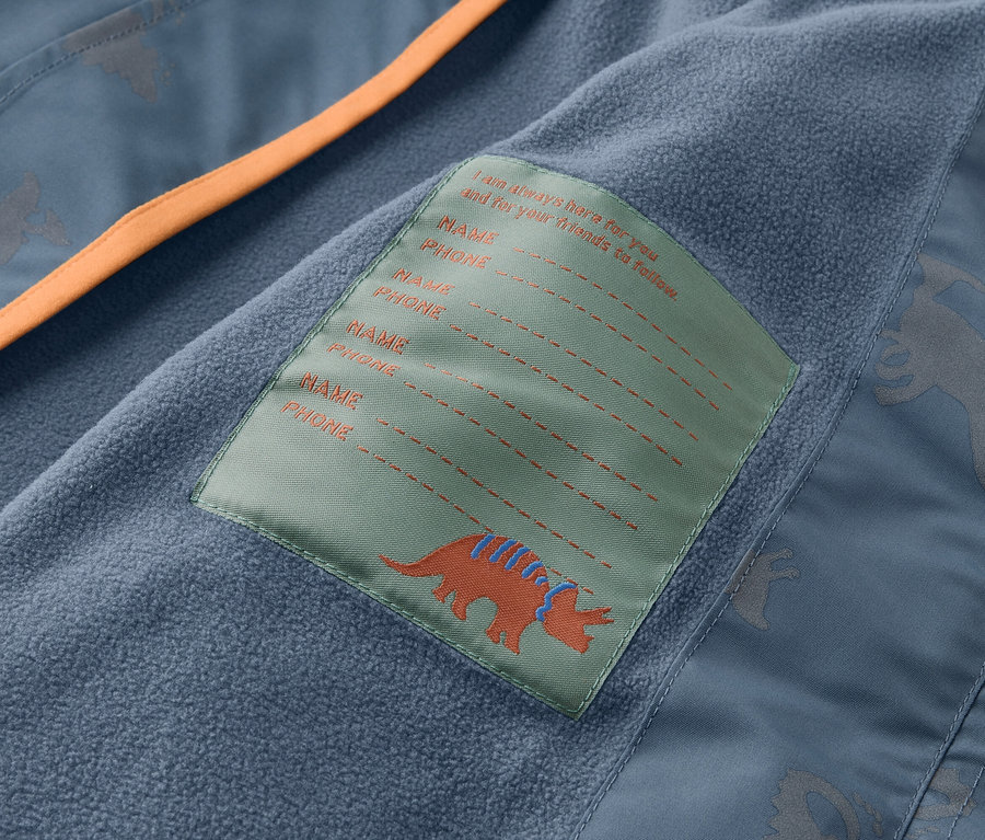 Innenansicht einer blauen Jacke mit orangefarbenem Saum und einem Etikett mit einem Dinosaurier und Platz für Namens- und Telefonnummerangaben.