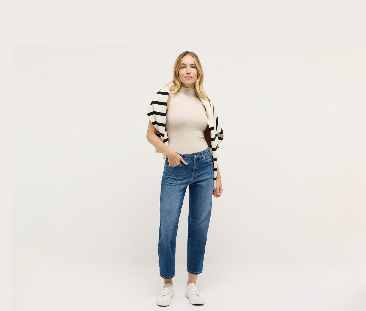 Frau in Angels Denim »Evi«, einem beigen Top und einer schwarz-weiß gestreiften Strickjacke.