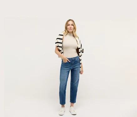 Frau in Angels Denim »Evi«, einem beigen Top und einer schwarz-weiß gestreiften Strickjacke.