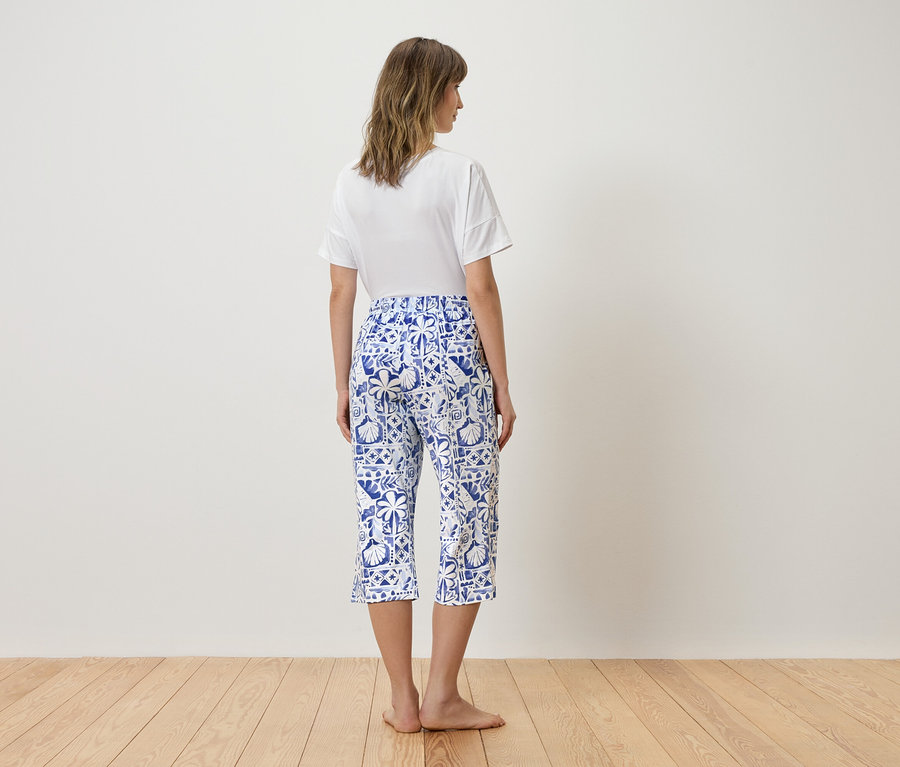 Frau von hinten in weißem T-Shirt und blauen, gemusterten Caprihosen.