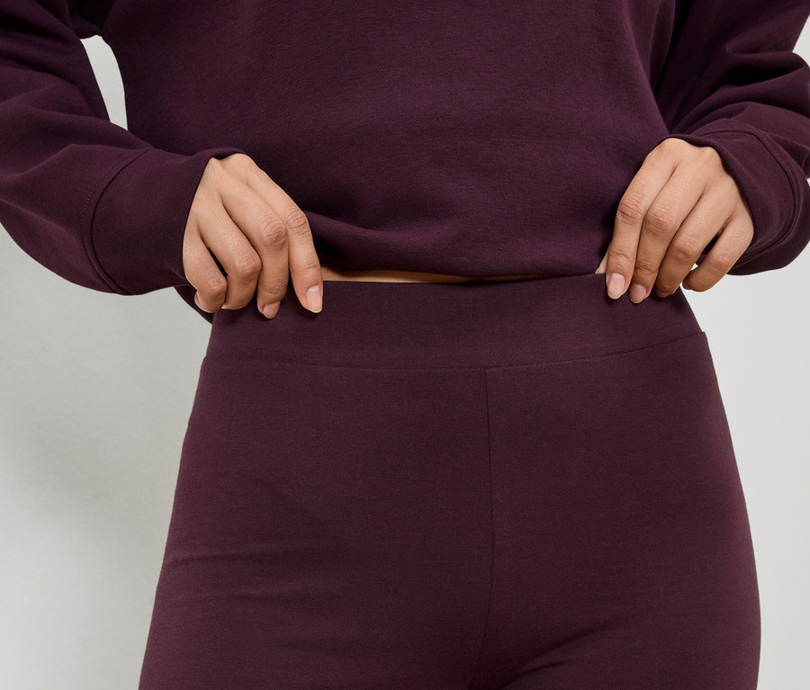 Nahaufnahme einer Person in bordeauxrotem Oberteil und Leggings, die den Bund der Leggings hält.
