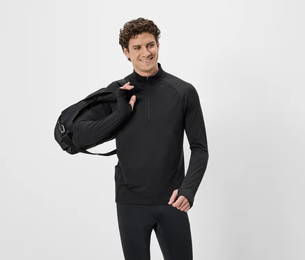 Mann mit lockigem Haar in schwarzem Sportoberteil mit Reißverschluss und schwarzer Hose, mit schwarzer Sporttasche über der Schulter.