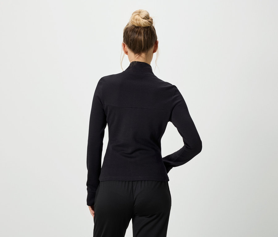 Rückenansicht einer Frau mit Duttfrisur, die ein schwarzes, langärmeliges Oberteil und eine schwarze Hose trägt.