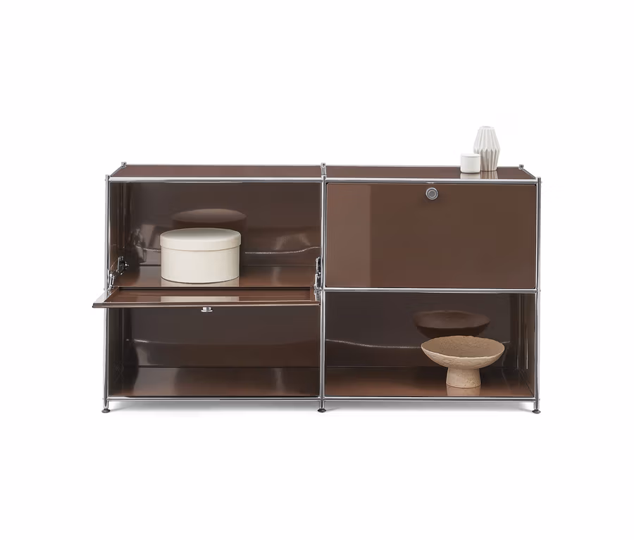 Ein braunes modulares Sideboard mit Chromrahmen. Die linke Seite hat ein offenes Fach mit einer weißen runden Box und eine teilweise geöffnete Tür unten. Die rechte Seite hat eine geschlossene Tür oben und ein offenes Fach unten mit zwei Dekoschalen. Zwei weiße Dekoobjekte stehen auf dem Sideboard.
