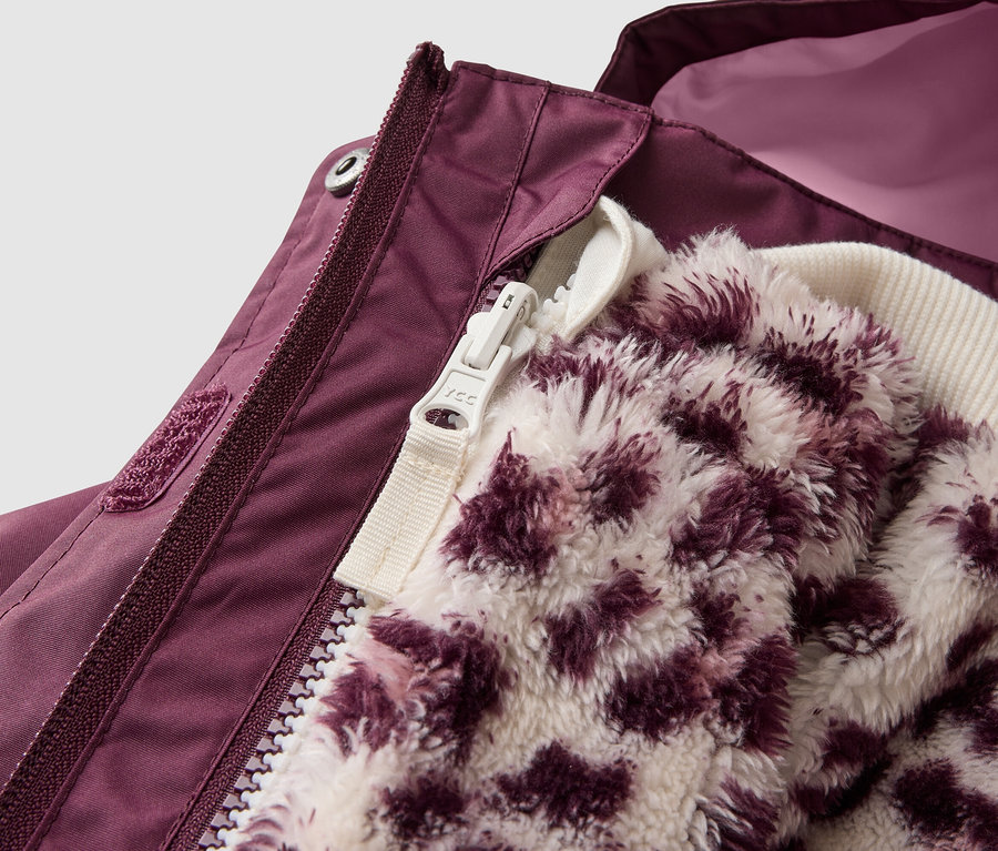 Nahaufnahme einer dunkelvioletten Jacke, die teilweise geöffnet ist und eine flauschige, weiß-violette Innenjacke mit Leopardenmuster zeigt. Die Außenjacke hat einen dunkelvioletten Reißverschluss und einen Klettverschluss, wobei ein helleres pinkes Futter sichtbar ist.