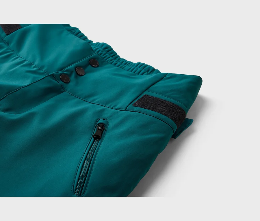 Nahaufnahme einer türkisfarbenen Hose mit drei schwarzen Knöpfen, einem elastischen Bund, einem schwarzen Klettverschluss und einer Reißverschlusstasche.