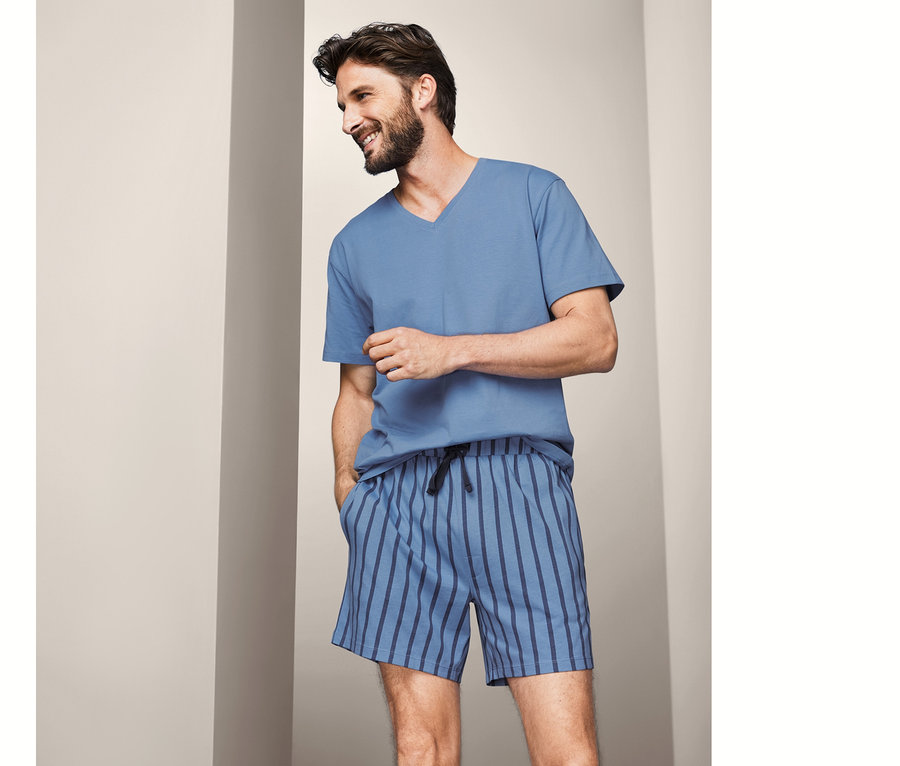 Mann trägt einen Shorty-Pyjama, unifarbenes Oberteil und gestreifte Shorts.