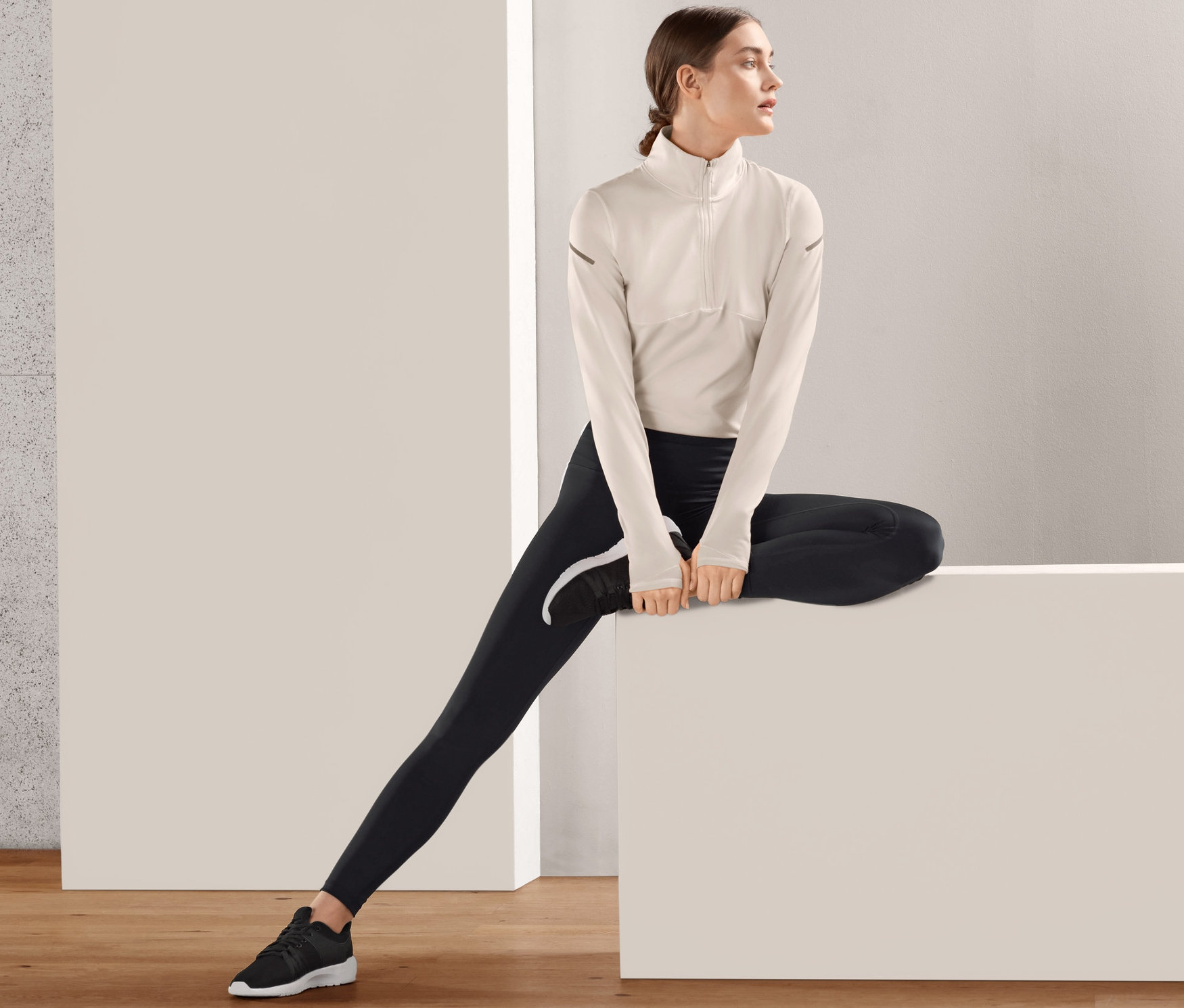 Frau sitzt auf einem weißen Block und trägt eine schwarze Sporttight.